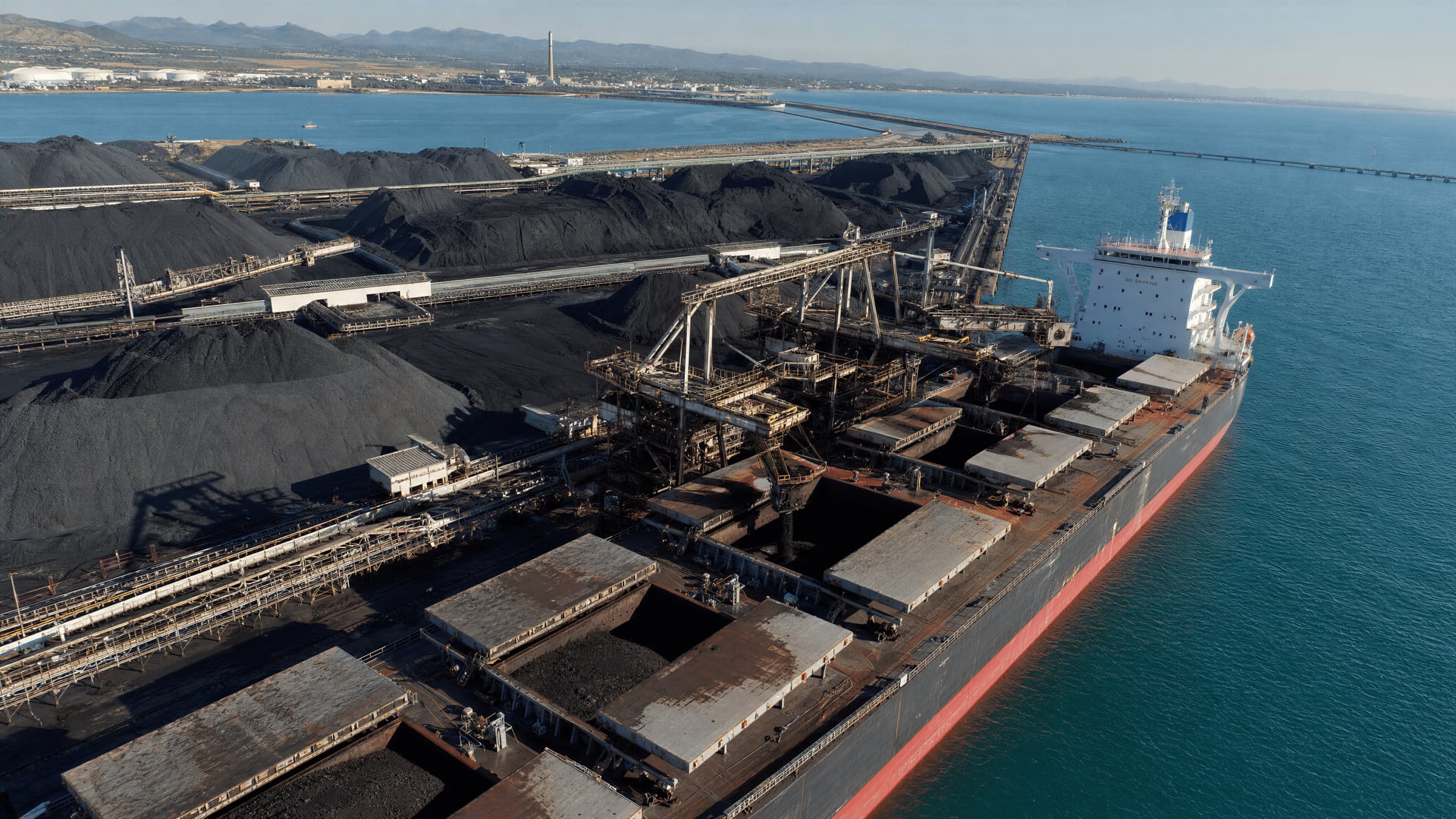 Australian coal export stockpiles and bulk carrier loading at a coastal terminal